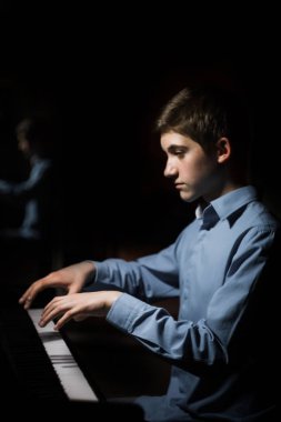 Genç adam piyanonun başında oturuyor. Erkek çocuk müzik okulunda klavye enstrümanı çalıyor. Öğrenci çalmayı öğreniyor. Eller piyanist. Siyah siyah arka plan. dikey