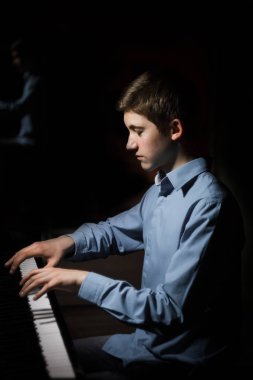 Genç adam piyanonun başında oturuyor. Erkek çocuk müzik okulunda klavye enstrümanı çalıyor. Öğrenci çalmayı öğreniyor. Eller piyanist. Siyah siyah arka plan. dikey