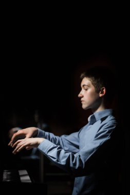 Genç adam piyanonun başında oturuyor. Erkek çocuk müzik okulunda klavye enstrümanı çalıyor. Öğrenci çalmayı öğreniyor. Eller piyanist. Siyah siyah arka plan. dikey