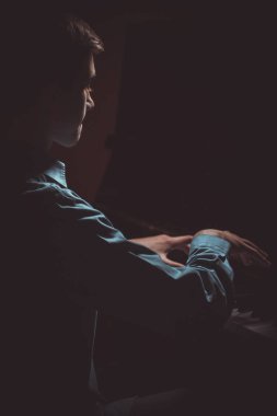 Genç adam piyanonun başında oturuyor. Erkek çocuk müzik okulunda klavye enstrümanı çalıyor. Öğrenci çalmayı öğreniyor. Eller piyanist. Siyah siyah arka plan. dikey