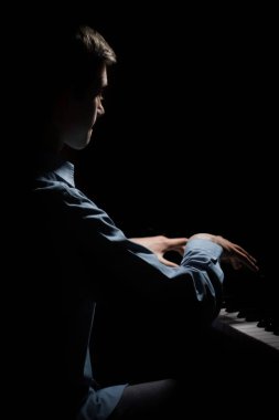 Genç adam piyanonun başında oturuyor. Erkek çocuk müzik okulunda klavye enstrümanı çalıyor. Öğrenci çalmayı öğreniyor. Eller piyanist. Siyah siyah arka plan. dikey