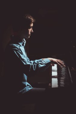 Genç adam piyanonun başında oturuyor. Erkek çocuk müzik okulunda klavye enstrümanı çalıyor. Öğrenci çalmayı öğreniyor. Eller piyanist. Siyah siyah arka plan. dikey
