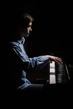Genç adam piyanonun başında oturuyor. Erkek çocuk müzik okulunda klavye enstrümanı çalıyor. Öğrenci çalmayı öğreniyor. Eller piyanist. Siyah siyah arka plan. dikey
