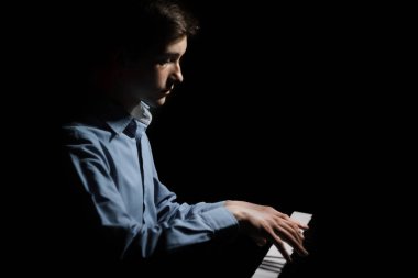 Genç adam piyanonun başında oturuyor. Erkek çocuk müzik okulunda klavye enstrümanı çalıyor. Öğrenci çalmayı öğreniyor. Eller piyanist. siyah arkaplan