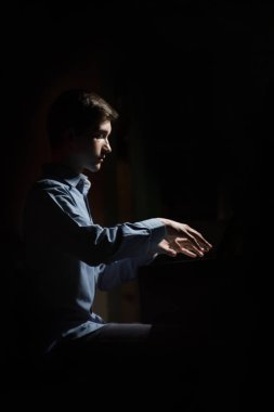Genç adam piyanonun başında oturuyor. Erkek çocuk müzik okulunda klavye enstrümanı çalıyor. Öğrenci çalmayı öğreniyor. Eller piyanist. Siyah siyah arka plan. dikey