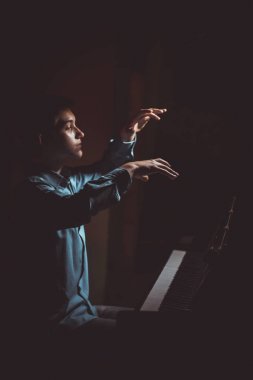 Genç adam piyanonun başında oturuyor. Erkek çocuk müzik okulunda klavye enstrümanı çalıyor. Öğrenci çalmayı öğreniyor. Eller piyanist. Siyah siyah arka plan. dikey