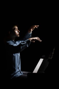 Genç adam piyanonun başında oturuyor. Erkek çocuk müzik okulunda klavye enstrümanı çalıyor. Öğrenci çalmayı öğreniyor. Eller piyanist. Siyah siyah arka plan. dikey