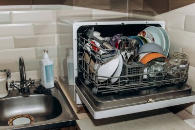 açık bulaşık makinesi, temiz yıkanmış bulaşıklarla tıkanmış kapatın. kuru çatal bıçak takımı yakın çekim. kaşık çatal. kupalar, tabaklar. mutfakta ev aletleri