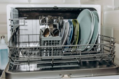 açık bulaşık makinesi, temiz yıkanmış bulaşıklarla tıkanmış kapatın. kuru çatal bıçak takımı yakın çekim. kaşık çatal. kupalar, tabaklar. mutfakta ev aletleri