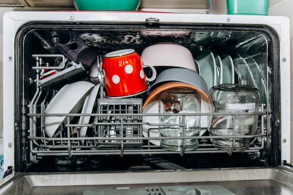 open dishwasher close up clogged with clean washed dishes. dry cutlery closeup. spoons forks. mugs, plates. household appliances in the kitchen