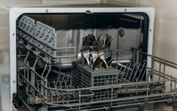 clean dry forks and spoons in an open dishwasher closeup. cutlery compartment close-up. household appliances in the kitchen