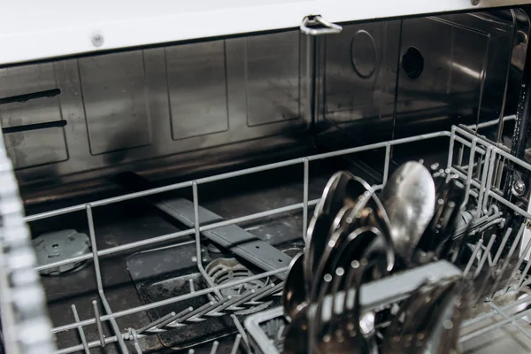 clean dry forks and spoons in an open dishwasher closeup. cutlery compartment close-up. household appliances in the kitchen