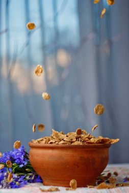 bir seramik kase yakından üst görünümünde düşen şeker mısır gevreği. pencereye karşı mavi çiçekler yakın çekim ile masaya dağılmış hafif kahvaltı. gıda fast cooking. sağlıklı gıda, diyet. Dikey