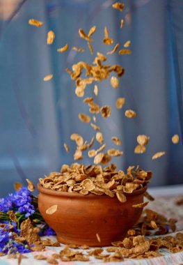 bir seramik kase yakından üst görünümünde düşen şeker mısır gevreği. pencereye karşı mavi çiçekler yakın çekim ile masaya dağılmış hafif kahvaltı. gıda fast cooking. sağlıklı gıda, diyet. Dikey