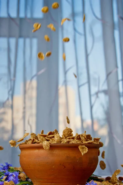 Fallende ZuckerCornflakes in einer Keramikschüssel Nahaufnahme von oben. Licht Frühstück auf dem Tisch mit blauen Blumen in Großaufnahme gegen das Fenster gestreut. Fast Food Kochen. gesunde Ernährung, Ernährung. vertikal — Stockfoto