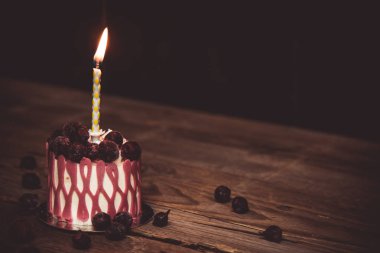 koyu bir arka plan üzerinde rustik ahşap masada kiraz meyve ile şenlikli bir pasta pasta bir yanan mum. kopyalama alanını kapatın. tatlı tartlet üzerinde vintage desen. doğum günü tatili