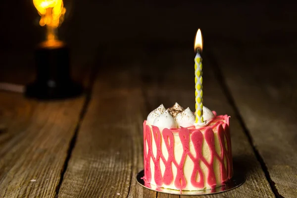 Eine brennende Kerze in einer festlichen Torte mit Kirschfrüchten auf einem rustikalen Holztisch vor dunklem Hintergrund. Kopierraum schließen. Vintage-Muster auf Desserttörtchen. Geburtstagsfeiertag — Stockfoto