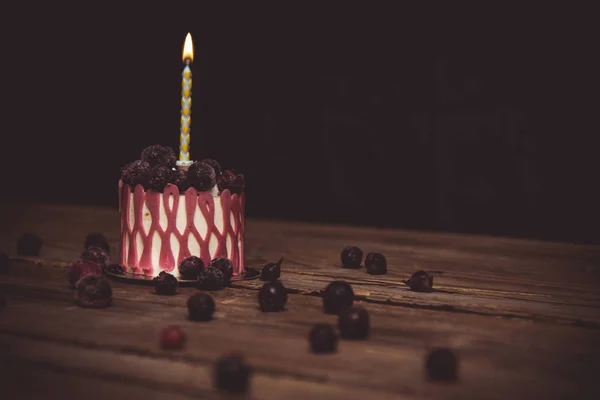Uma vela ardente em um bolo festivo com frutas de cereja em uma mesa de madeira rústica em um fundo escuro. fechar espaço de cópia. padrão vintage na tartete de sobremesa. feriado de aniversário — Fotografia de Stock