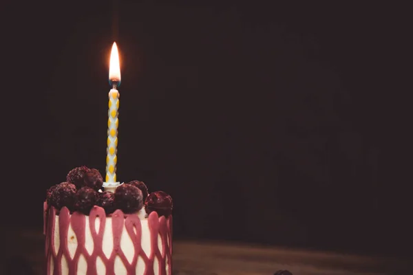 Ett brinnande ljus i en festlig tårtkaka med körsbärs frukter på ett rustikt träbord på en mörk bakgrund. Stäng kopierings utrymmet. Vintage mönster på dessert tartlet. Födelsedag semester — Stockfoto