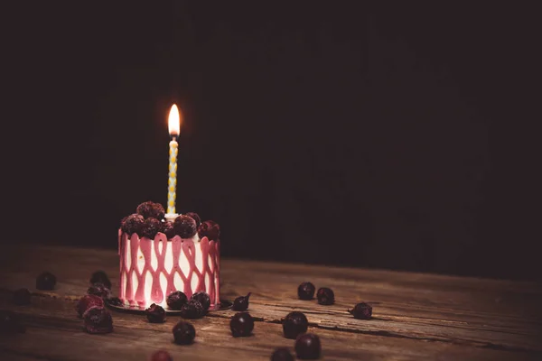 One burning candle in a festive cake cake with cherry fruits on a rustic wooden table on a dark background. close up copy space. vintage pattern on dessert tartlet. birthday holiday — Stock Photo, Image