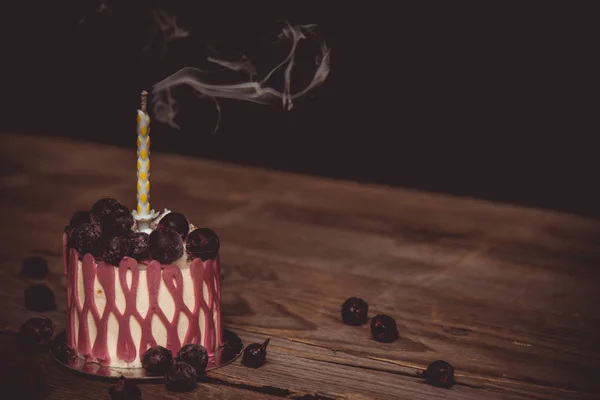 Uma vela extinta em um bolo festivo com os frutos de cereja em uma mesa de madeira rústica em um fundo escuro. fechar espaço de cópia. padrão vintage na tartete de sobremesa. feriado de aniversário — Fotografia de Stock