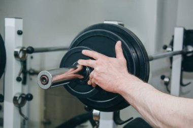 büyük elleri olan bir atlet eğitim merkezinde eğitim aparatları için metal diskler tarafından ağırlık ekler. spor salonunda eğitim ekipmanları yakın çekim