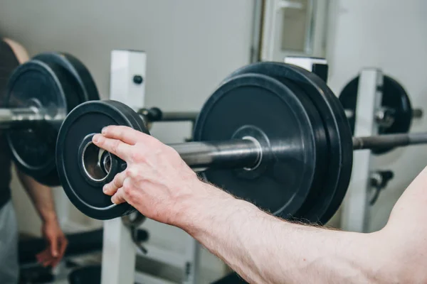 Büyük elleri olan bir atlet eğitim merkezinde eğitim aparatları için metal diskler tarafından ağırlık ekler. spor salonunda eğitim ekipmanları yakın çekim — Stok fotoğraf