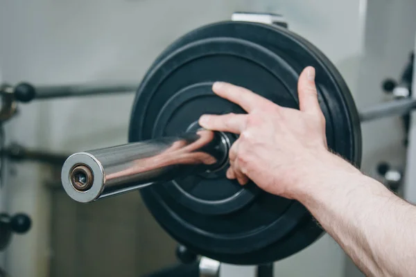 Ein Athlet mit großen Händen fügt dem Trainingsgerät im Trainingszentrum Gewicht durch die Metallscheiben hinzu. Trainingsgeräte in der Turnhalle aus nächster Nähe — Stockfoto
