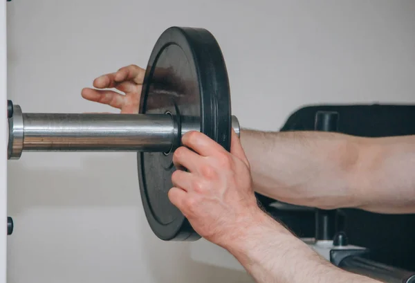 Um atleta com mãos grandes acrescenta peso pelos discos metálicos ao aparelho de treinamento no centro de treinamento. equipamento de formação no ginásio close-up — Fotografia de Stock
