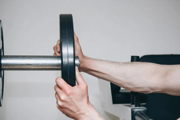 En idrottare med stora händer lägger vikt av metall skivorna till tränings apparaten i Training Center. träningsutrustning i gymmet närbild — Stockfoto