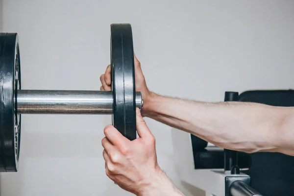 큰 손을 가진 운동 선수는 훈련 센터의 훈련 장치에 금속 디스크에 의해 무게를 추가합니다. 체육관 클로즈업에서 훈련 장비 — 스톡 사진