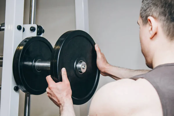 En idrottare med stora händer lägger vikt av metall skivorna till tränings apparaten i Training Center. träningsutrustning i gymmet närbild — Stockfoto