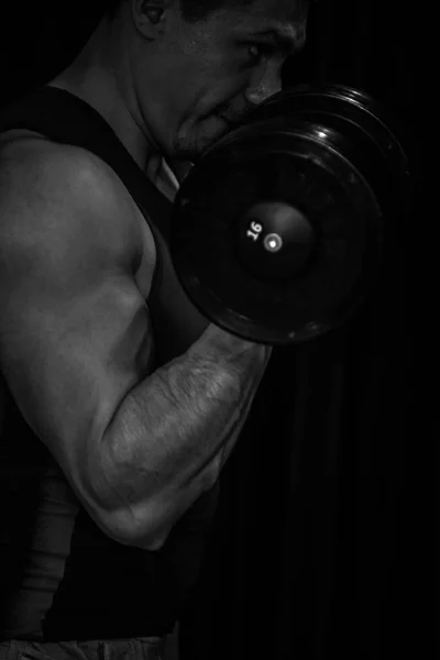 Atleet voert biceps handen met dumbbells in het centrum van trainingen op een zwarte achtergrond. trainingstools in de Gym close-up — Stockfoto