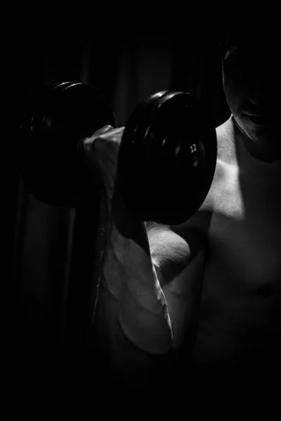 Αθλητής τρένα δικέφαλα χέρια με βαράκια στο κέντρο των προπονήσεων σε μαύρο φόντο. εκπαιδευτικά εργαλεία στο κοντινό γυμναστήριο — Φωτογραφία Αρχείου