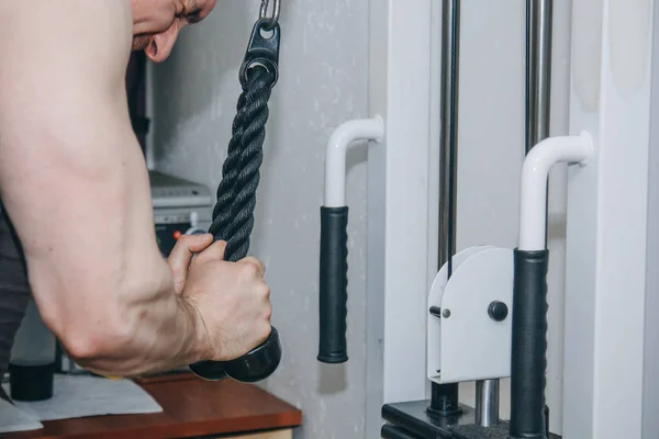 Atleta treina mãos tríceps com uma máquina de treinamento no centro de treinamento em um fundo preto. ferramentas de treinamento no ginásio close-up — Fotografia de Stock