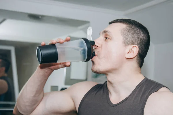 the athlete drinks water from a shaker in the training center. rest between exercises in the gym
