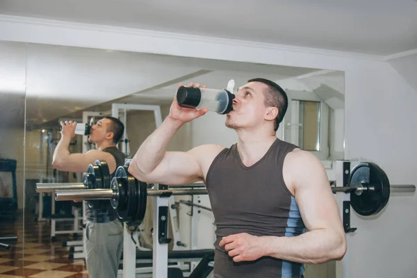 Sportovec pije vodu z třepačky ve výcvikových centrech. odpočinek mezi cvičeními v tělocvičně — Stock fotografie