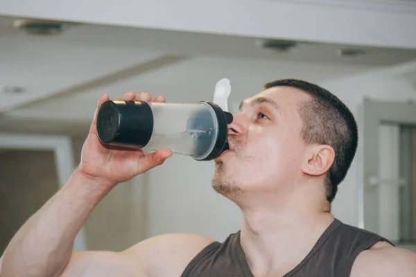 the athlete drinks water from a shaker in the training center. rest between exercises in the gym