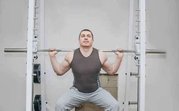 Um atleta bem treinado treina seus músculos das pernas em um centro de treinamento. agachamentos barbell no ginásio — Fotografia de Stock