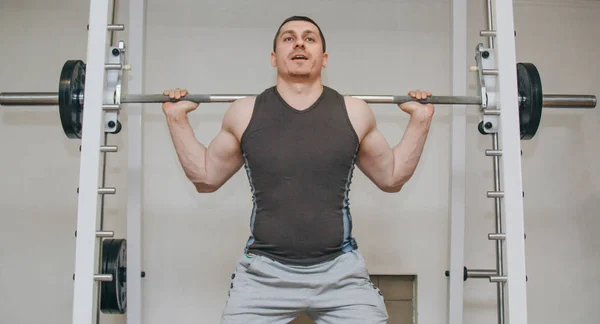 Ein durchtrainierter Sportler trainiert seine Beinmuskulatur in einem Trainingszentrum. Hantelhocken in der Turnhalle — Stockfoto