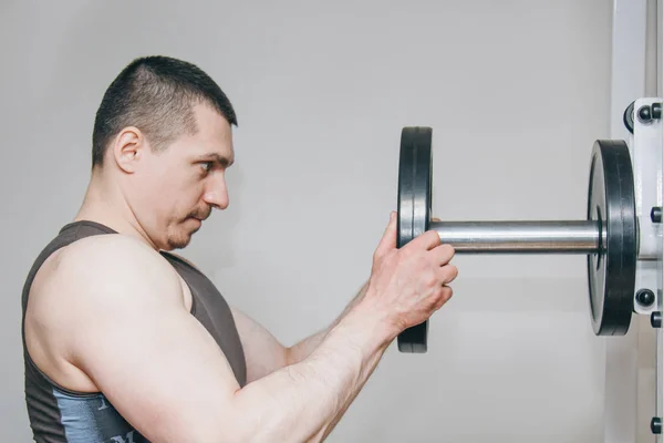En idrottare med stora händer lägger vikt av metall skivorna till tränings apparaten i Training Center. träningsutrustning i gymmet närbild — Stockfoto