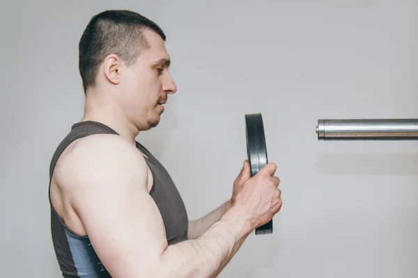 Un athlète avec de grandes mains ajoute du poids par les disques métalliques à l'appareil d'entraînement dans le centre d'entraînement. équipement d'entraînement dans le gymnase close-up — Photo