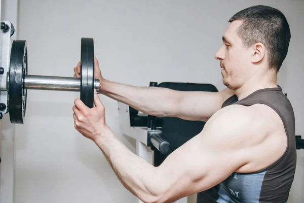 Ein Athlet mit großen Händen fügt dem Trainingsgerät im Trainingszentrum Gewicht durch die Metallscheiben hinzu. Trainingsgeräte in der Turnhalle aus nächster Nähe — Stockfoto