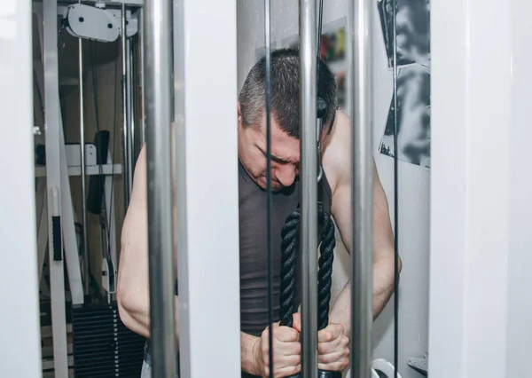 Atleta treina mãos tríceps com uma máquina de treinamento no centro de treinamento em um fundo preto. ferramentas de treinamento no ginásio close-up — Fotografia de Stock