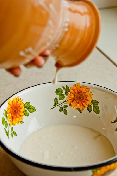 Женская рука наливает молоко из керамической посуды в металлическую чашу. покрашенный в белую эмаль, коричневый кувшин глиняной посуды вблизи. вертикальная — стоковое фото