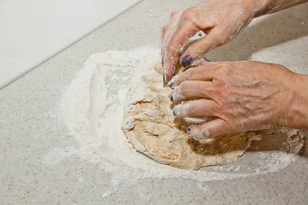 Las manos femeninas amasan la masa con harina sobre una mesa de cocina blanca. Vista superior. etapa de preparación para hornear, cocinar —  Fotos de Stock