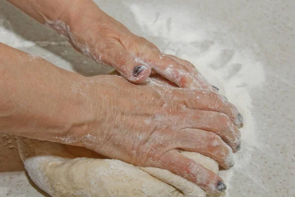 Las manos femeninas amasan la masa con harina sobre una mesa de cocina blanca. Vista superior. etapa de preparación para hornear, cocinar — Foto de Stock