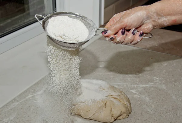Θηλυκό αλεύρι κοσκινίσματος μέσα από ένα σουρωτήρι χέρι για το αλεύρι σε ένα λευκό τραπέζι κουζίνας κοντά στο χώρο αντιγραφής. Μαγειρική ζύμη. μεταλλική συσκευή κουζίνας — Φωτογραφία Αρχείου