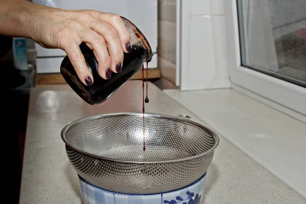 Жіночі руки насипали варення з банки в миску через сито на фоні інтер'єру кухні. випічка, приготування їжі — стокове фото