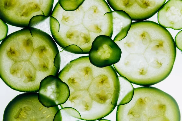 Fatias translúcidas verdes de pepino no fundo da luz branca brilhante close-up. discos transparentes de legumes. textura dos padrões caleidoscópicos na macro — Fotografia de Stock